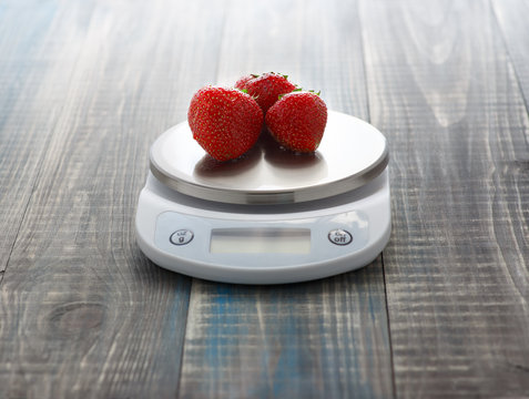 Three ripe washed strawberries lie on digital kitchen scales
