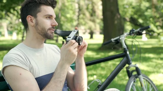 Handsome man sitting in the park and doing photos on old camera, steadycam shot
