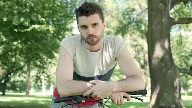 Handsome man leaning on the bicycle's frame and doing serious look to the camera, steadycam shot
