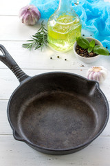 Frying pan made of cast iron and spices on a white wooden kitchen table. Culinary background.
