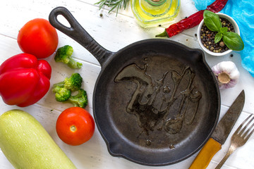 Frying pan made of cast iron, various fresh vegetables and spices on a white wooden kitchen table. Culinary background.
