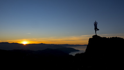 Silhouette young woman practicing yoga on top mountain at sunset