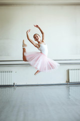 Cute little ballerina in pink ballet costume and pointe shoes is dancing in the room. Kid in dance class. Child girl is studying ballet. Copy space. © Kseniia