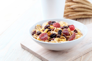 cornflakes and dry berry fruits in a white bowl on a wooden background.