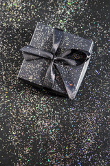 Black gift box with a bow and sparkles around on a black background