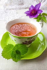 Herbal tea with a slice of lemon and a sprig of aromatic mint on a tablecloth in a rural style and a flower clematis. The concept of a romantic morning breakfast in the summer