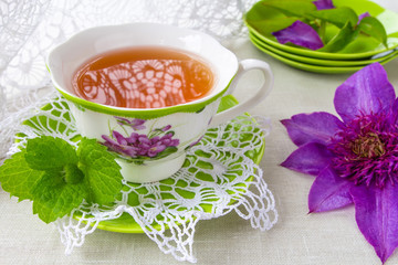 Herbal tea with a slice of lemon and a sprig of aromatic mint on a tablecloth in a rural style and a flower clematis. The concept of a romantic morning breakfast in the summer
