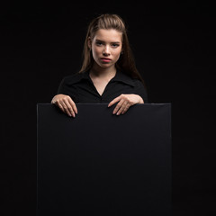 Young sexy woman portrait of a confident businesswoman showing presentation, pointing placard black background. Ideal for banners, registration forms, presentation, landings, presenting concept..