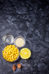  Raw ingredients for classic hummus. Hummus ingredients. Chickpeas, lemon juice, olive oil, garlic, pepper, sesame, tahini.  Top view. Space for text.