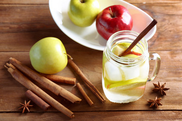 Mason jar with fresh apple water and cinnamon on wooden table
