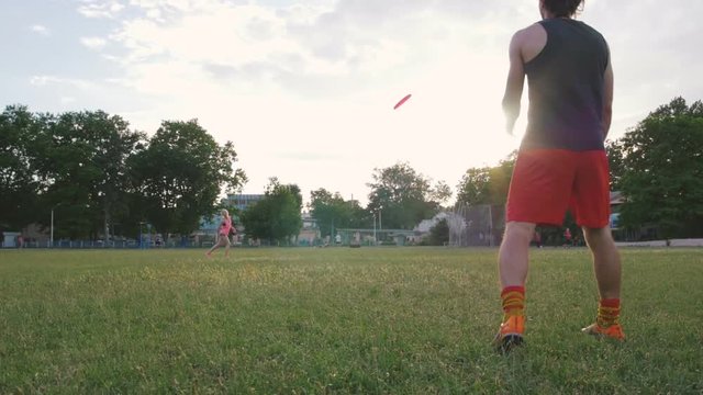 young man and woman playing frisbee in the park during sunset, slow motion