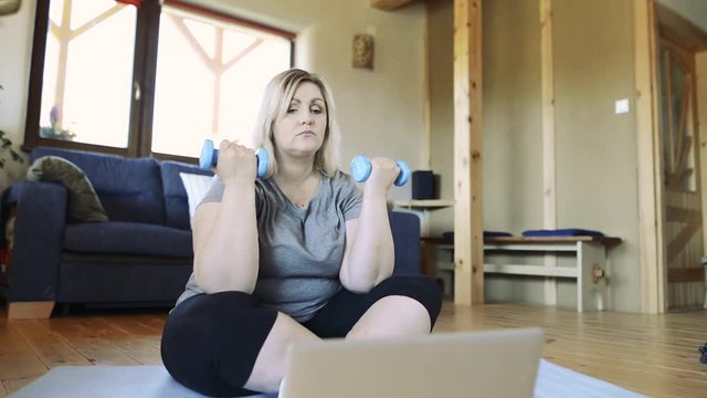 Attractive overweight woman at home working out with barbells.