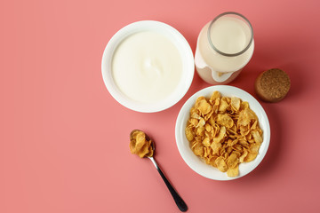 Corn flakes and yogurt in white bowl  with milk bottle place on pink background