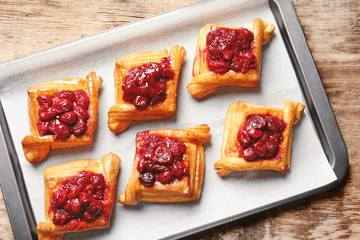 Tray with delicious puff pastries and cherry on wooden table