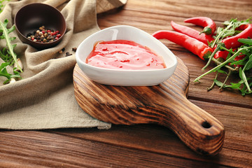 Tasty chili sauce in bowl on wooden board
