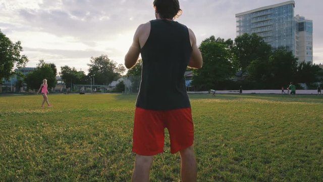 young man and woman playing frisbee in the park during sunset, slow motion
