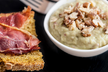 Bread, ham, nuts and avocado paste breakfast on black background