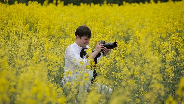 Photographer with a camera taking pictures in a blooming yellow field
