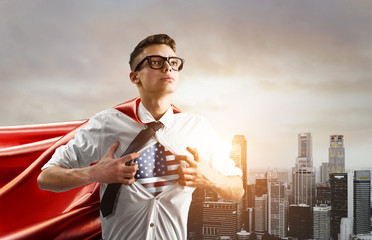 USA Superhero. Young businessman showing American flag under his shirt against sunset city.