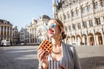 Poster Jonge vrouw die & 39 s ochtends met wafel een traditioneel Belgisch gebak in het centrum van de stad Brussel loopt © rh2010