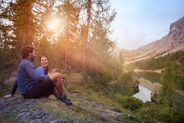 Smiling happy man and woman couple enjoy lake panorama view with sun flare light. Group of friends...