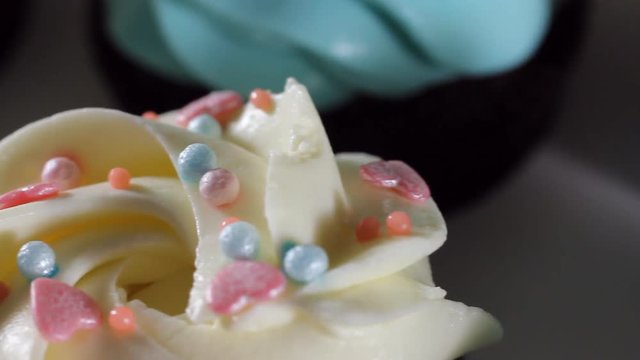 Sliding camera shooting. Close-up of blue and white cream on mafin. Icing sugar being sieved on pink frosted cupcake in slow motion
