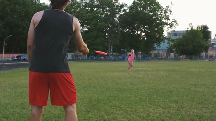 young man and woman playing frisbee in the park during sunset, slow motion - Powered by Adobe
