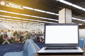 Laptop computer with white blank screen on wooden table with blurred in airport terminal waiting room, selective focus, copy space, working outside office, online social media, searching data concept
