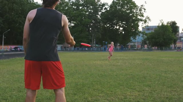 young man and woman playing frisbee in the park during sunset, slow motion