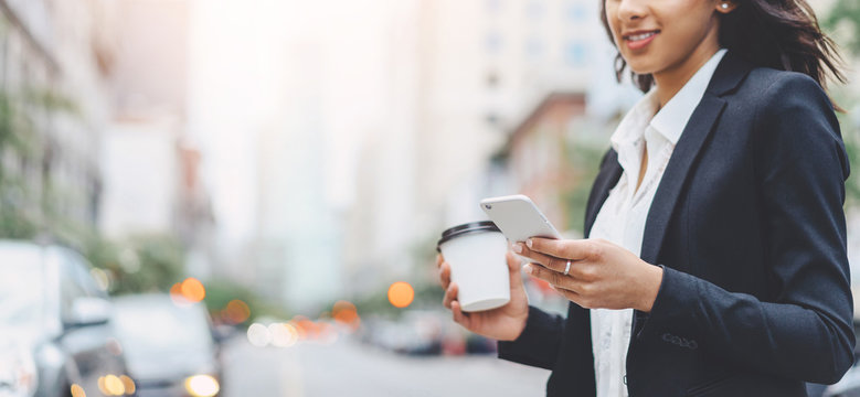 Cropped Image Of Successful Business Woman Wearing Suit Using Modern Smartphone And Drinking Coffee To Go Before Going To Work Early In The Morning