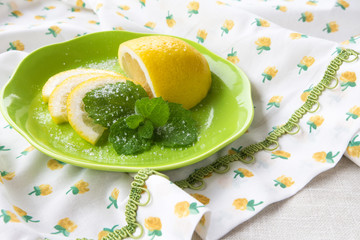 Fresh juicy citrus tropical fruit slices of lemon and a sprig of mint on a light green salad on a tablecloth. The concept of a healthy vitamin dietary diet of a vegetarian lifestyle