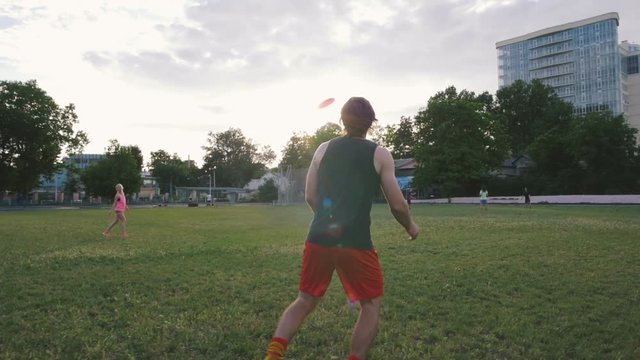 young man and woman playing frisbee in the park during sunset, slow motion