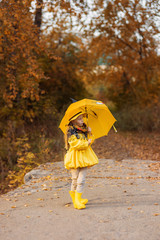 Cute little girl in a yellow raincoat with a yellow umbrella in an autumn park