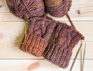 Fototapeta na wymiar Mittens knitted in dark brown wool on the needles wooden background