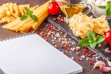 Ingredients for pasta with mozzarella and tomatoes on a dark background, horizontally with a notepad for writing, copyspace