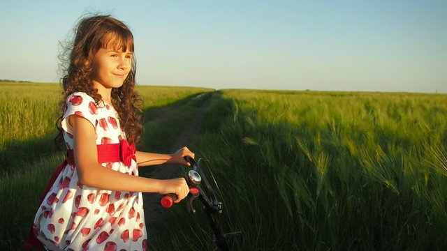 Child on a bicycle near a wheat field. Beautiful little girl on a bicycle in the countryside.