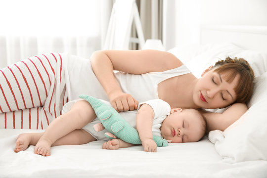 Young woman with cute sleeping baby lying on bed at home