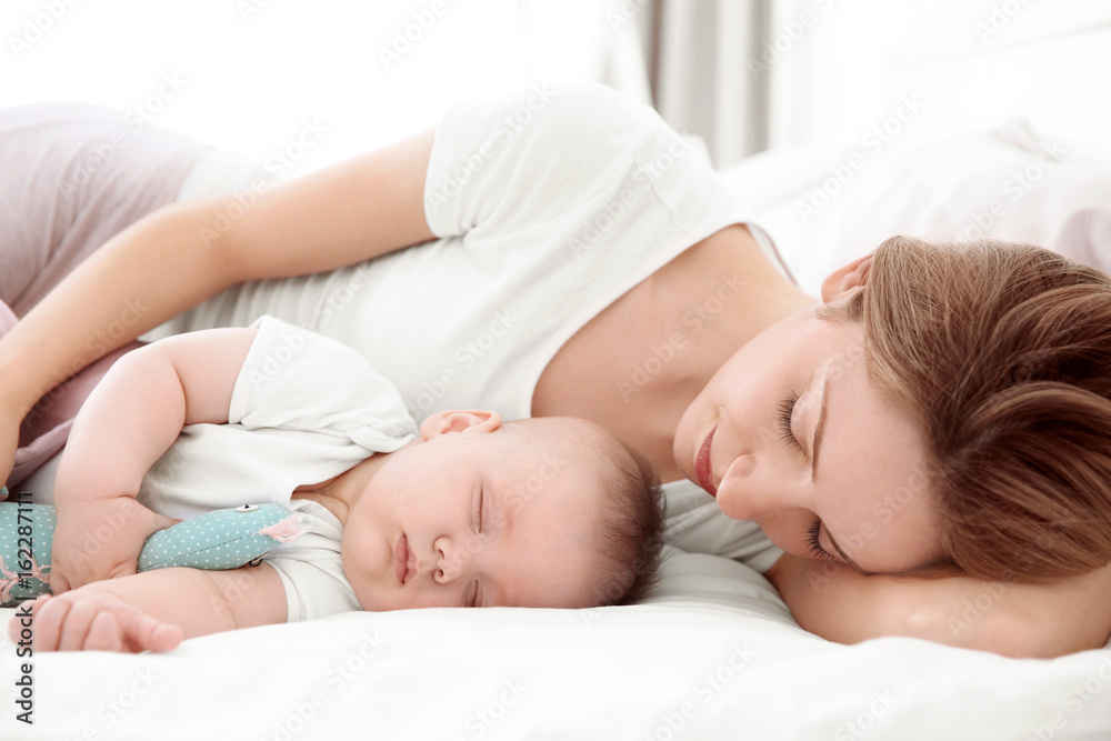 Wall mural Young woman with cute baby sleeping on bed at home