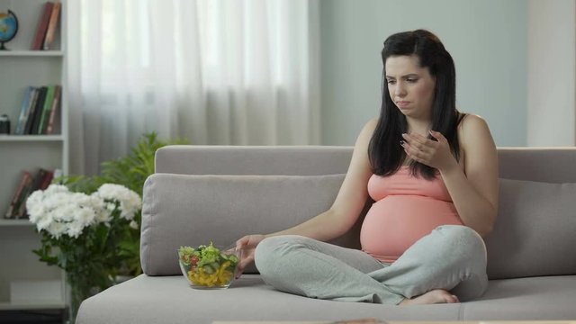 Pregnant girl eating vegetable salad, feeling sickness, suffering toxicosis