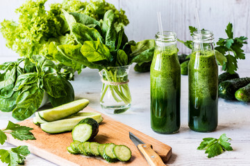 Detox diet. Two small bottles of fresh green smoothies with ingredients on a light wooden background.