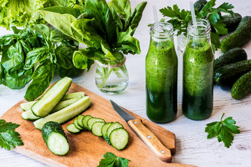 Detox diet. Two small bottles of fresh green smoothies with ingredients on a light wooden background.