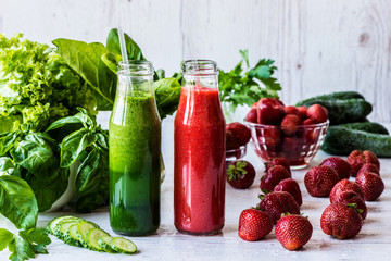 Green smoothie and strawberry smoothie in two small bottles with ingredients on a light wooden background. Healthy detox drinks.