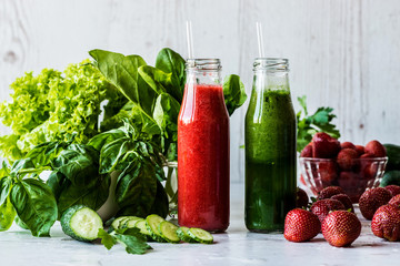 Green smoothie and strawberry smoothie in two small bottles with ingredients on a light wooden background. Healthy detox drinks.