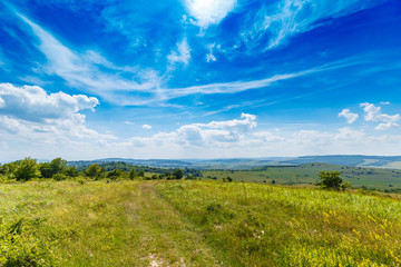 Obraz premium Green grass, rural road and clouds