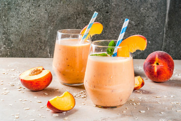 Healthy eating. Breakfast, snack. Drink smoothies from fresh peach, milk (yogurt) and oatmeal, decorated with mint leaves, with striped straws. On a light stone table. Copy space