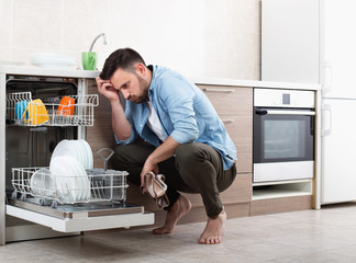 Tired man beside open dishwasher