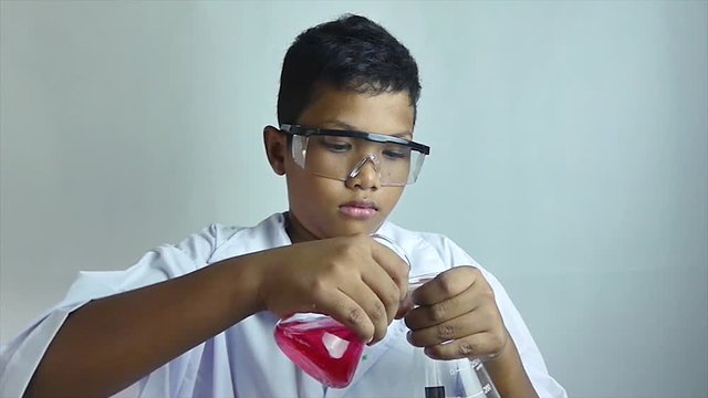 Close up slow motion of a multicultural ethnic boy pouring a reddish fluid into another beaker - the reaction causes a rush of bubbles, to his surprise and amazement