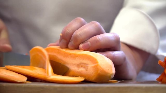 Chef cutting carrot with knife on the board