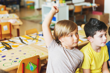 Two concentrated 4-5 year old boys in classroom, kid raising hand on lesson