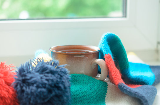 A Cup Of Tea On A Window Sill Wrapped In A Scarf. Warming Up The House.